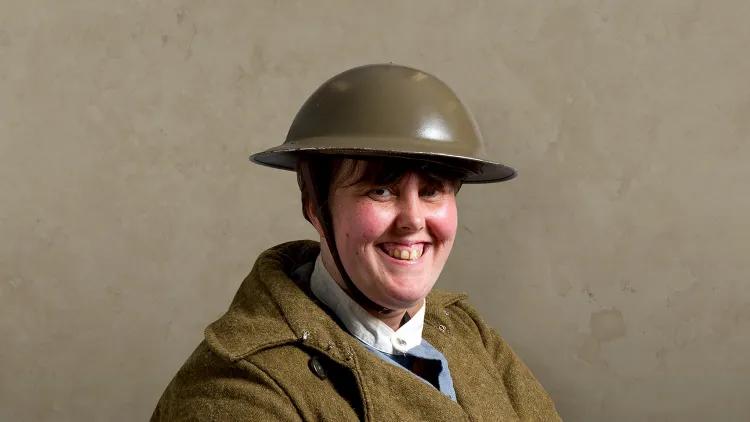 Woman wearing first world war tin helmet and khaki uniform and brown leather satchel