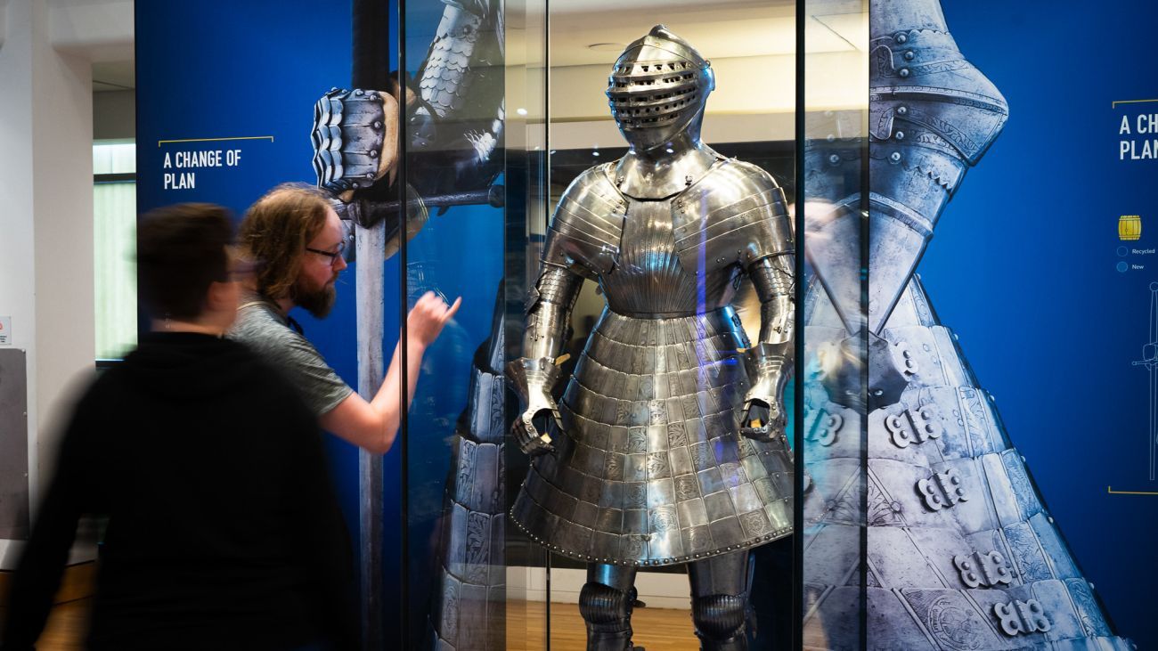 a couple stop to admire and examine a shining armour with a skirt that once belonged to Henry VIII